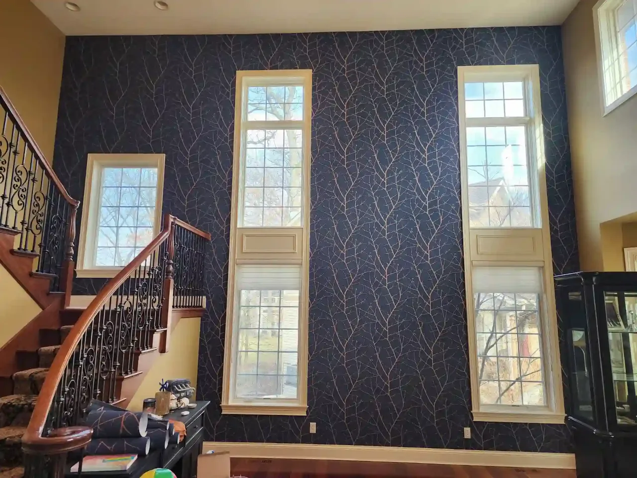 Dark navy branch-pattern wallpaper rising beside a tall stair hall